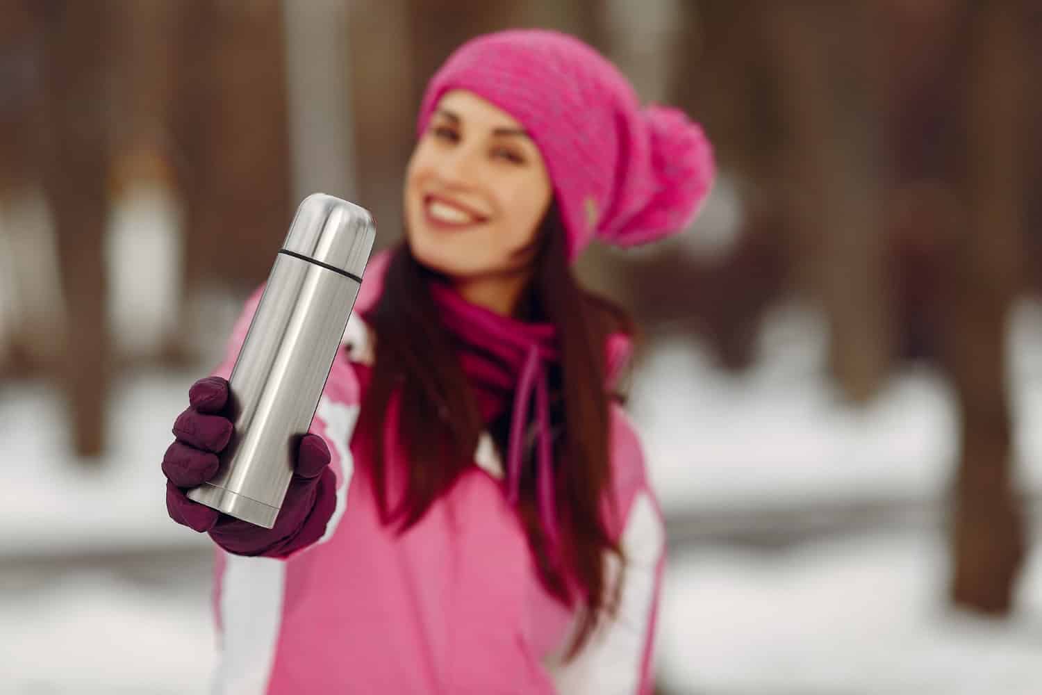 Woman in a winter park. Lady in pink sportsuit. Girl with a stainless steel bottle.